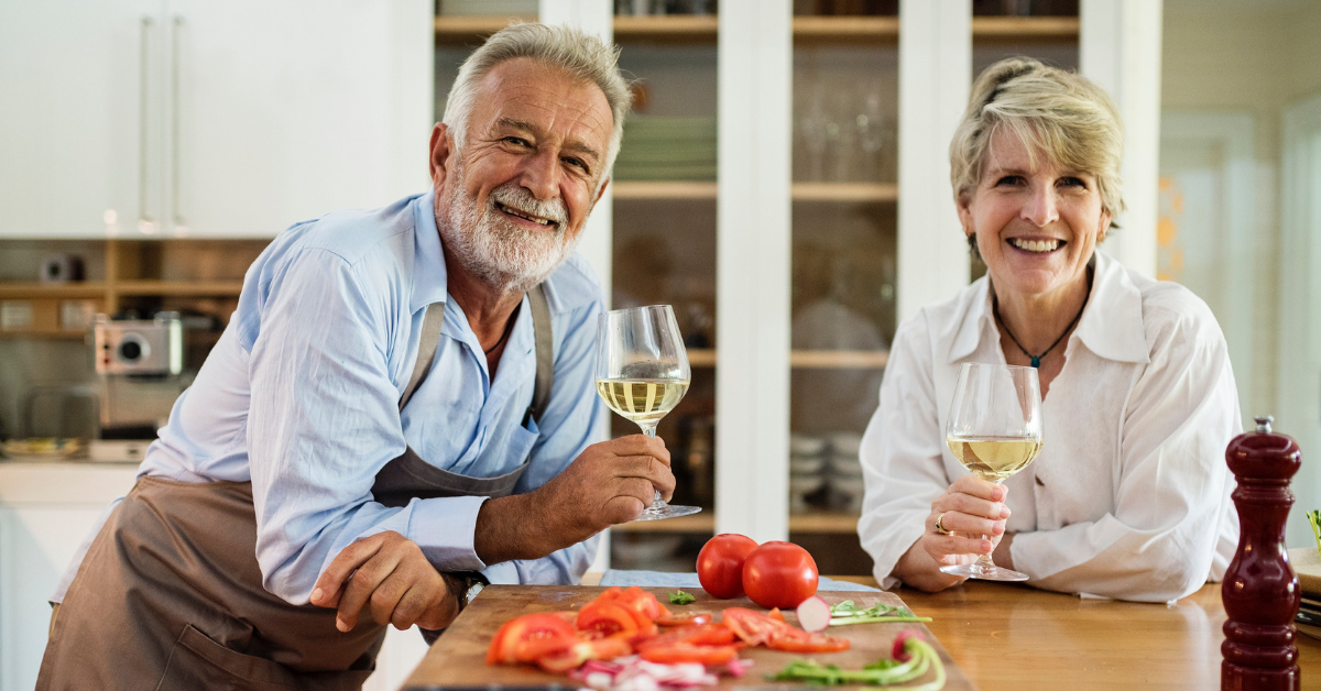 An older couple sharing white wine and making a salad